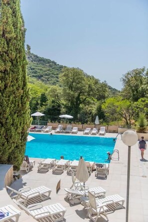 A swimming pool with lounge chairs and umbrellas, surrounded by greenery and hills.