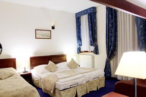 A hotel room with a double bed, a bedside table, a lamp, a window with curtains, and a radiator. - Hotel Patria (Zakopane)
