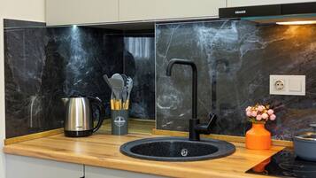 Una cocina moderna con un lavamanos negro, hervidor de acero inoxidable y un florero con flores.