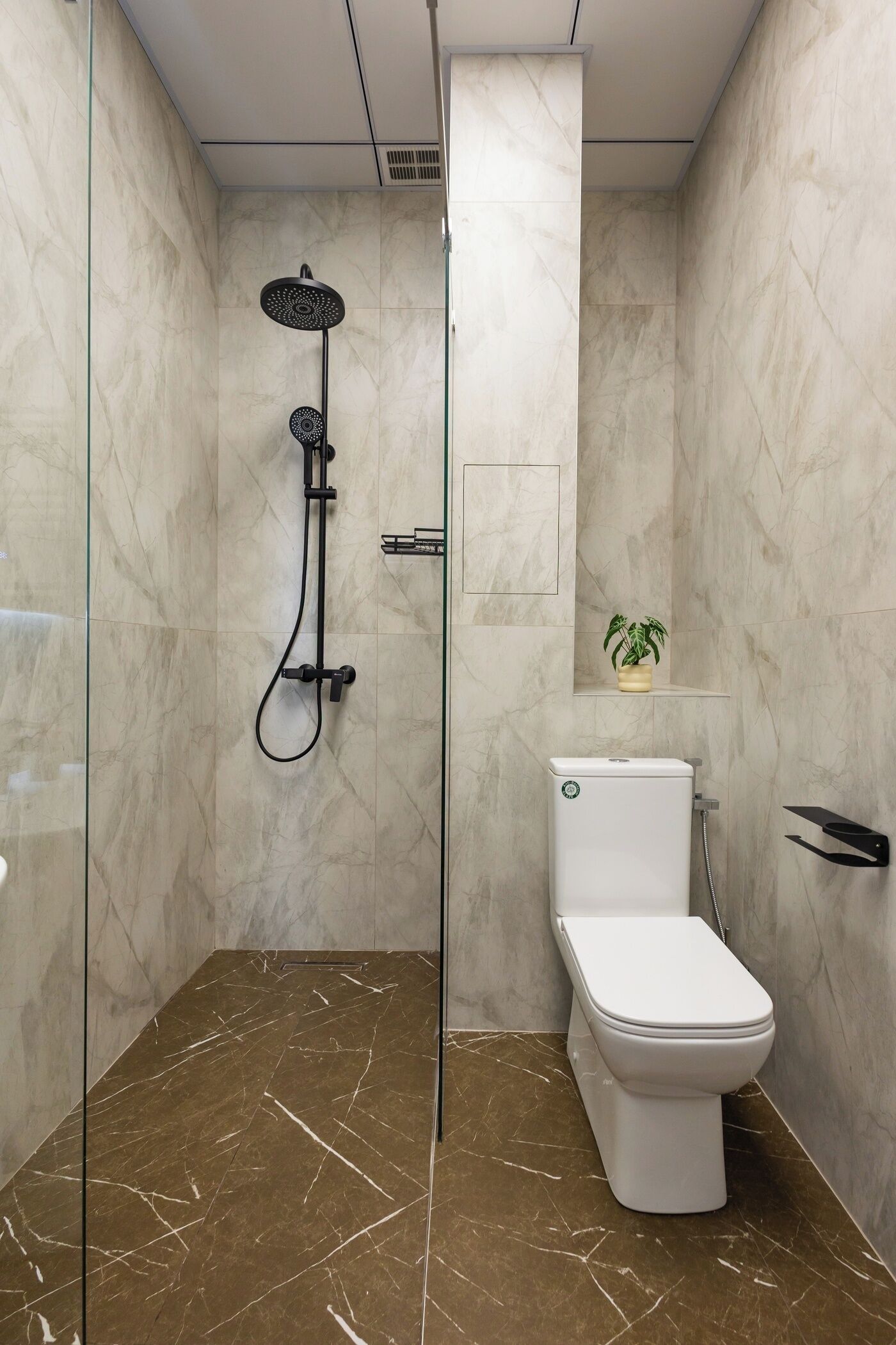 A modern bathroom with a glass-enclosed shower, a white toilet, and a marble floor.