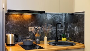 Une cuisine moderne avec un dosseret en marbre noir, une bouilloire en acier inoxydable, une plaque de cuisson à induction noire, un évier avec un robinet noir et un vase contenant des ustensiles.