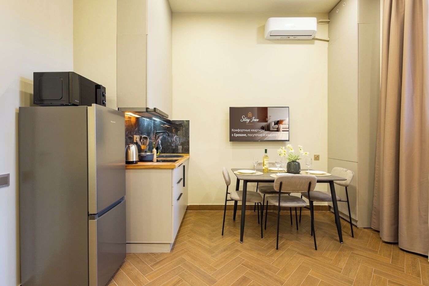 A compact kitchen with a refrigerator, microwave, and stove, a dining area with a table and chairs, and a mounted air conditioner.
