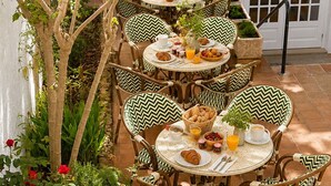 A patio with round tables and chairs, surrounded by greenery and a white wall.
