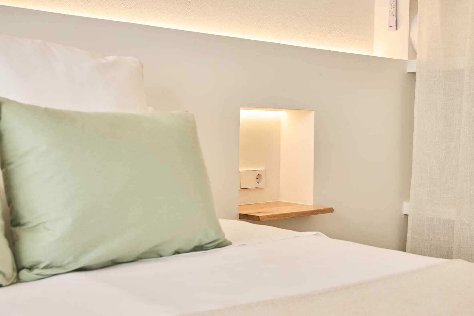 A hotel room with a bed, a bedside table, a mirror, and a wall socket.