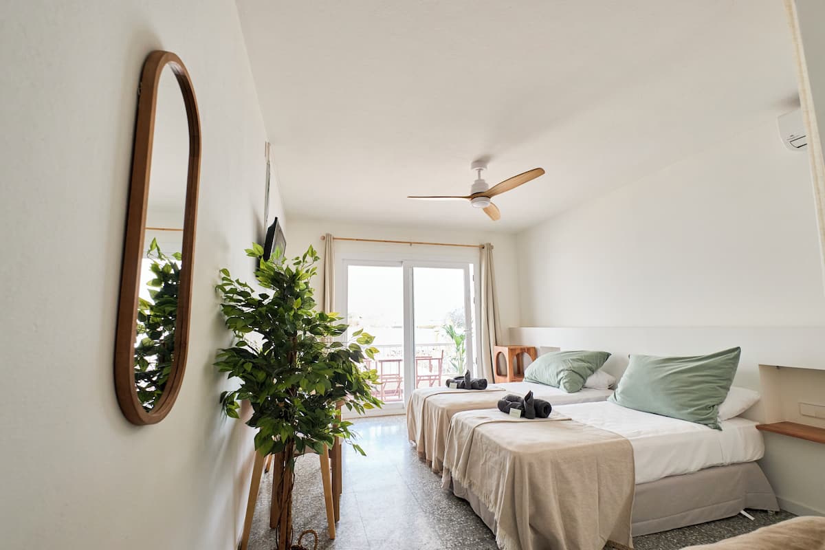 A bedroom with two beds, a ceiling fan, a large mirror, and a potted plant.