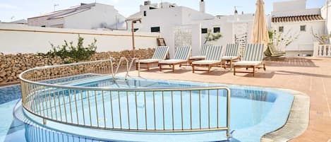 Una piscina con borde curvo, rodeada de sillas de descanso y un muro de piedra.