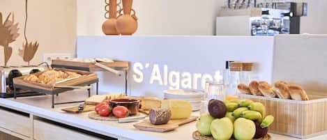 A breakfast buffet with bread, cheese, tomatoes, apples, and a sign reading 'S'Algaret'.