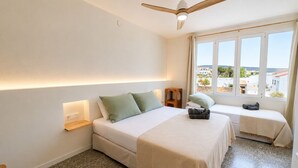 A bedroom with a bed, a bench, a ceiling fan, and a window with a view.