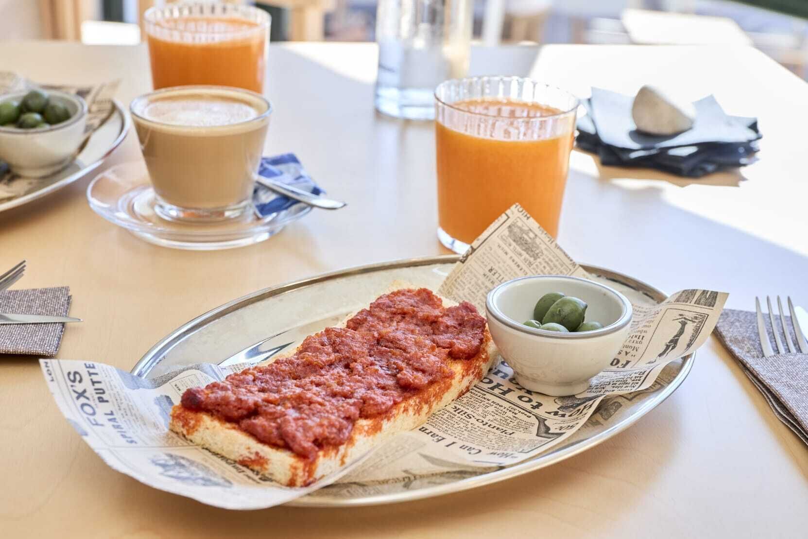 Un repas composé de bruschettas, d’un verre de jus d’orange et d’un bol d’olives, le tout servi sur une table.