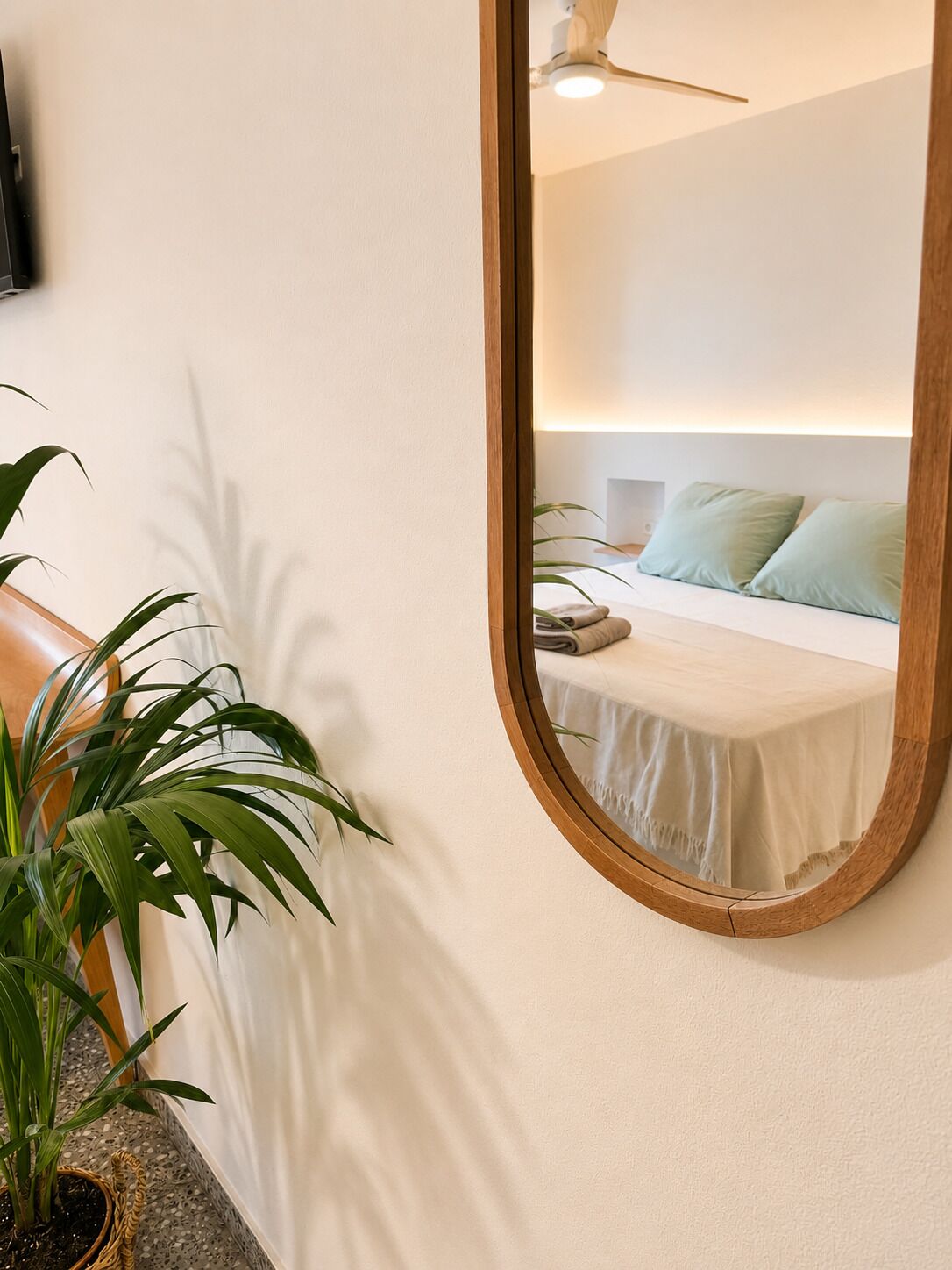 Ein Schlafzimmer mit Bett, Kissen, Nachttisch, Spiegel und Deckenventilator.