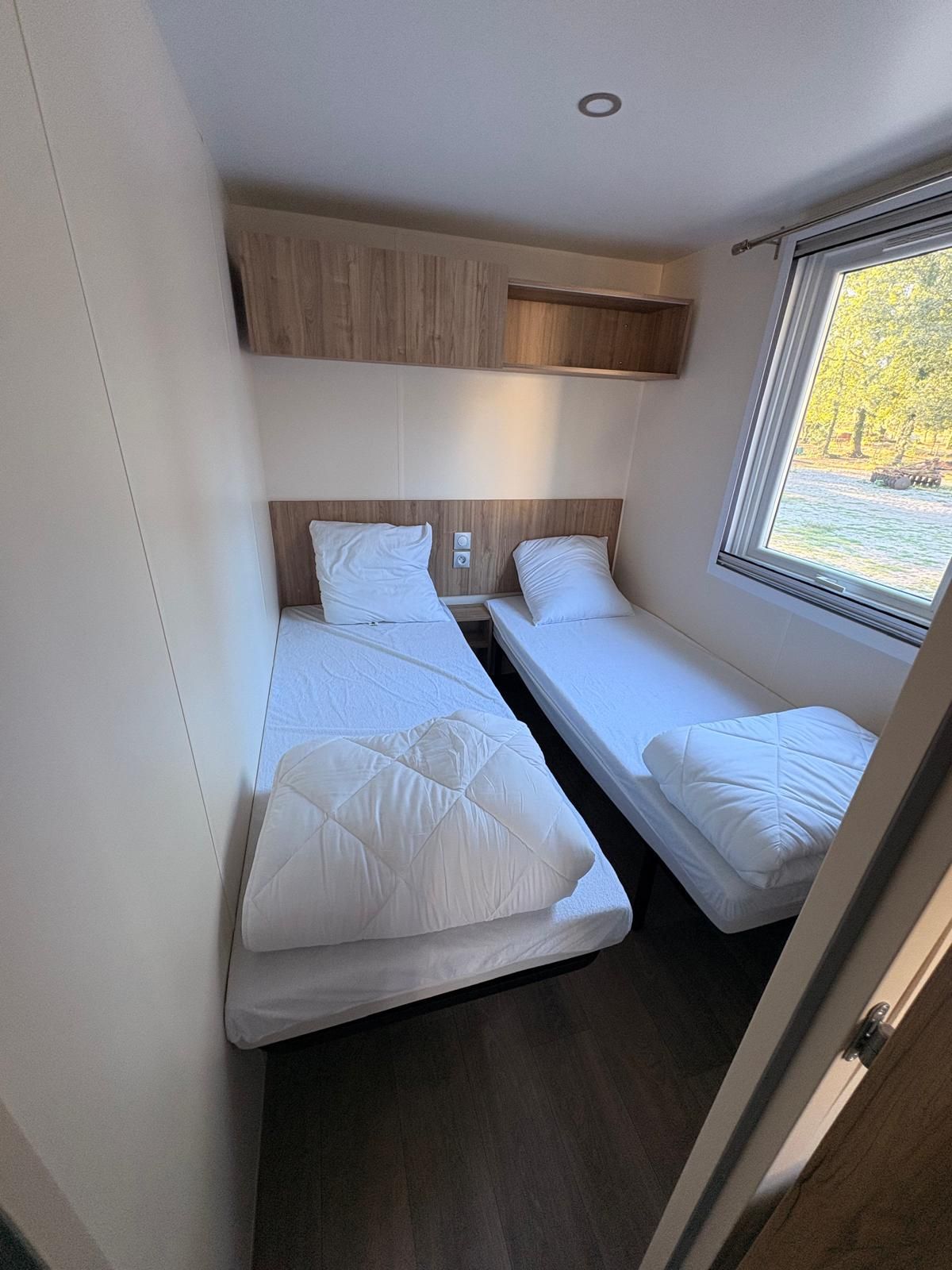 A compact room with two single beds, a wooden headboard, a small window, and a ceiling light.