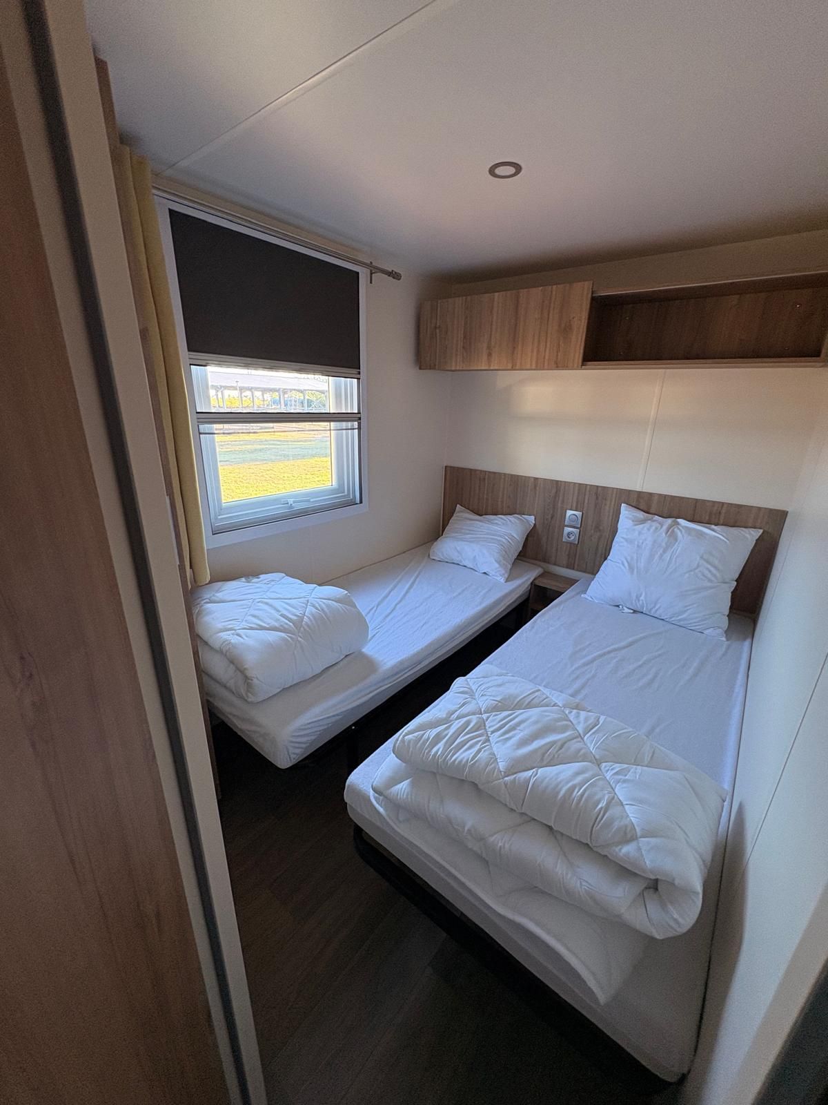 A compact bedroom with two single beds, a window with a view, and a wooden headboard.