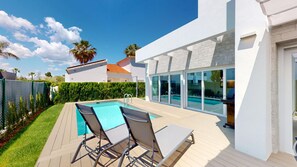Ein moderner Poolbereich im Freien mit zwei Liegestühlen, einem Holzdeck und einem Pool mit Glasveranda.