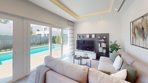 Ein modernes Wohnzimmer mit großem Fernseher, einer Couch, Blick auf einen Pool und einem Balkon.