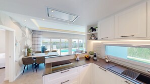 Eine moderne Küche mit weißen Schränken, ein Essbereich mit Tisch und Stühlen sowie Blick auf einen Swimmingpool.