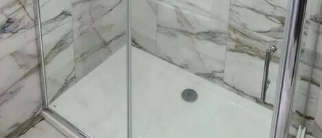 Una ducha con cerramiento de vidrio, paredes de mármol y suelo de baldosas.