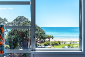 Blick aus einem Fenster auf einen Strand mit Palmen und einem wolkenlosen Himmel.