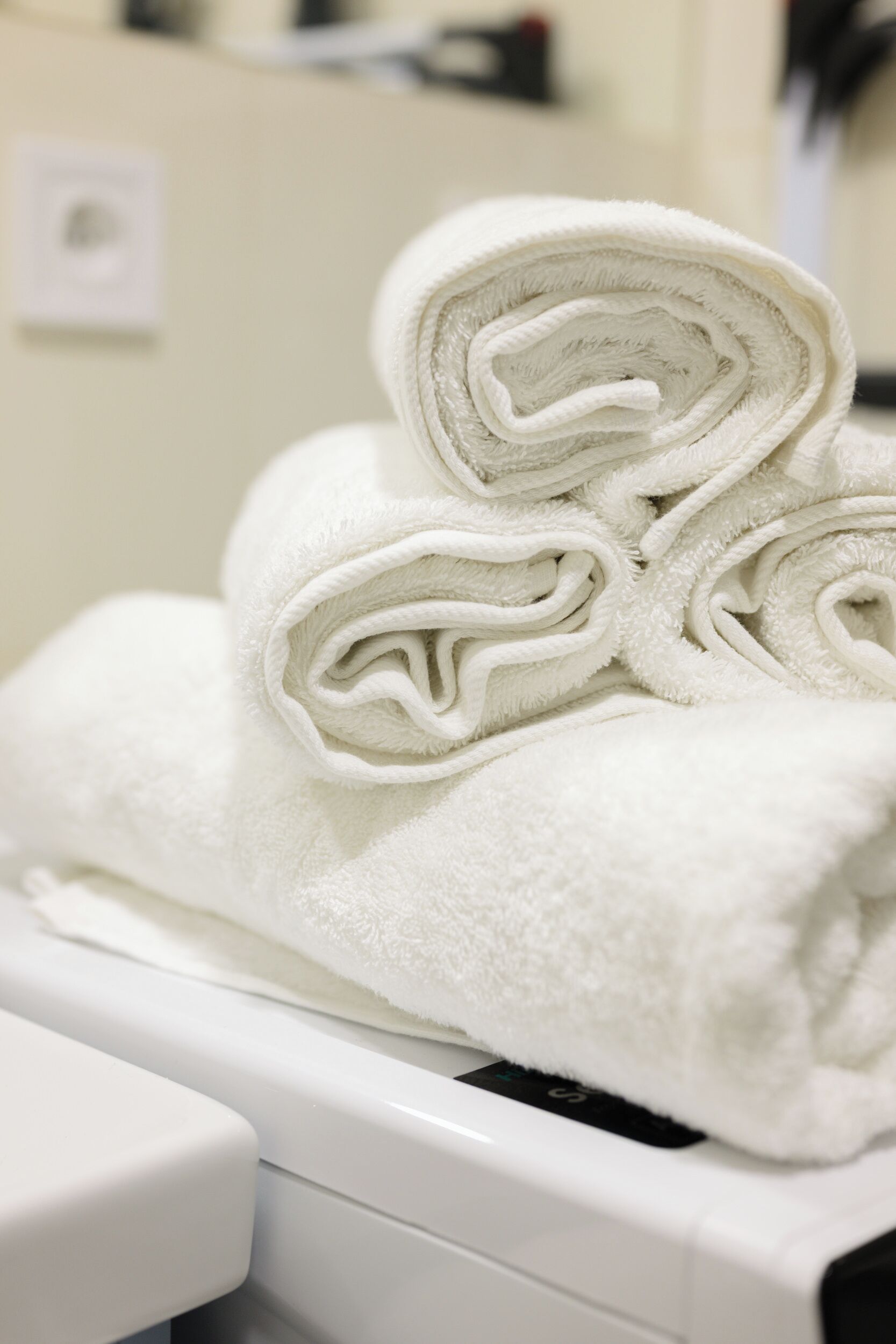 A stack of white towels on a white appliance, likely a dryer, in a room with a light-colored wall and a visible electrical outlet.