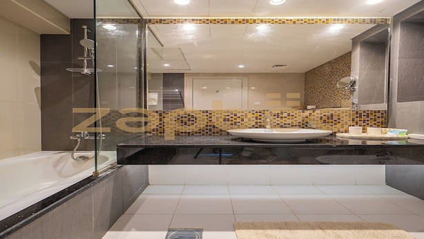 A modern bathroom with a glass shower enclosure, a bathtub, a vanity with a sink, and a mirror. - Stylish 1BR-Upper Crest Near Dubai Mall (Dubai)