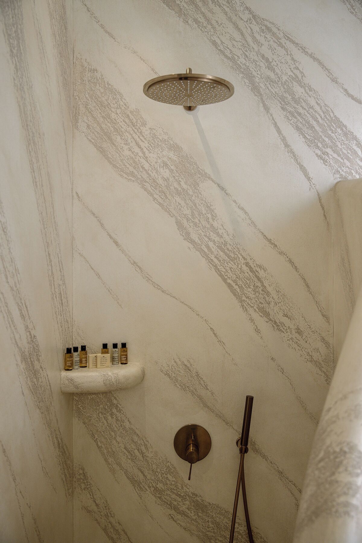A shower with a marble-like wall pattern, a handheld showerhead, and a shelf with toiletries.