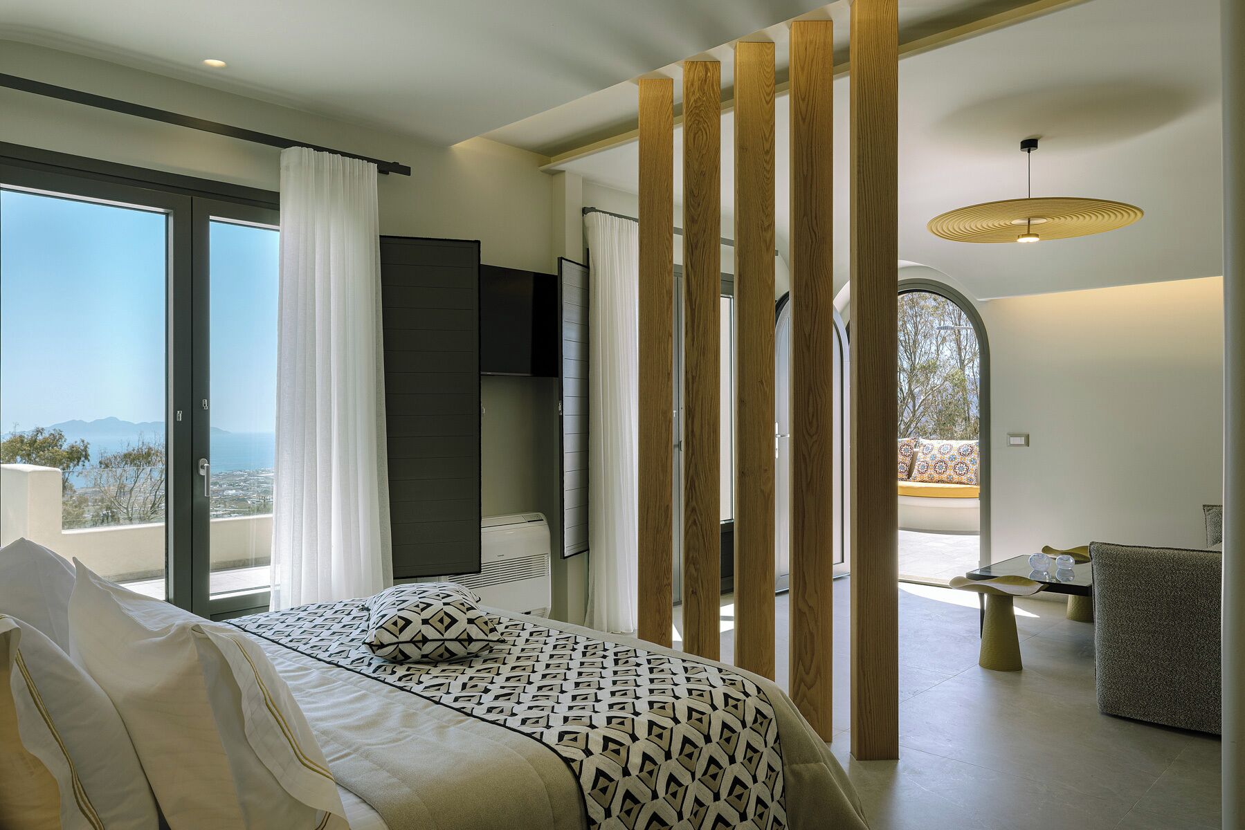 Quarto moderno com cama, televisão, varanda e área de refeições.