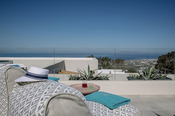 A terrace with a clear view of the sea, a table with drinks, and a patterned sofa.