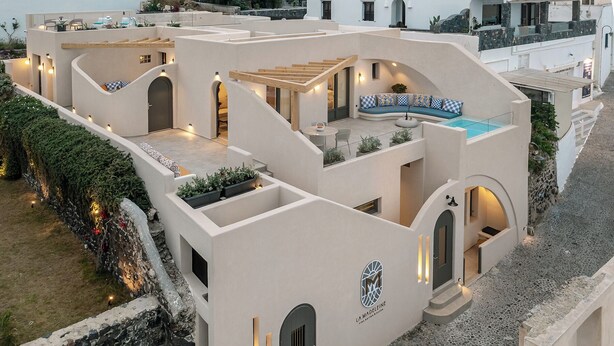 A modern building with multiple balconies, a pool, and a logo indicating it's a hotel. - La Madeleine Suites Fira (Santorini)