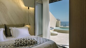 A bedroom with a bed, pillows, a bedside lamp, a view of the sea, and a balcony with a hot tub. - La Madeleine Suites Fira (Santorini)
