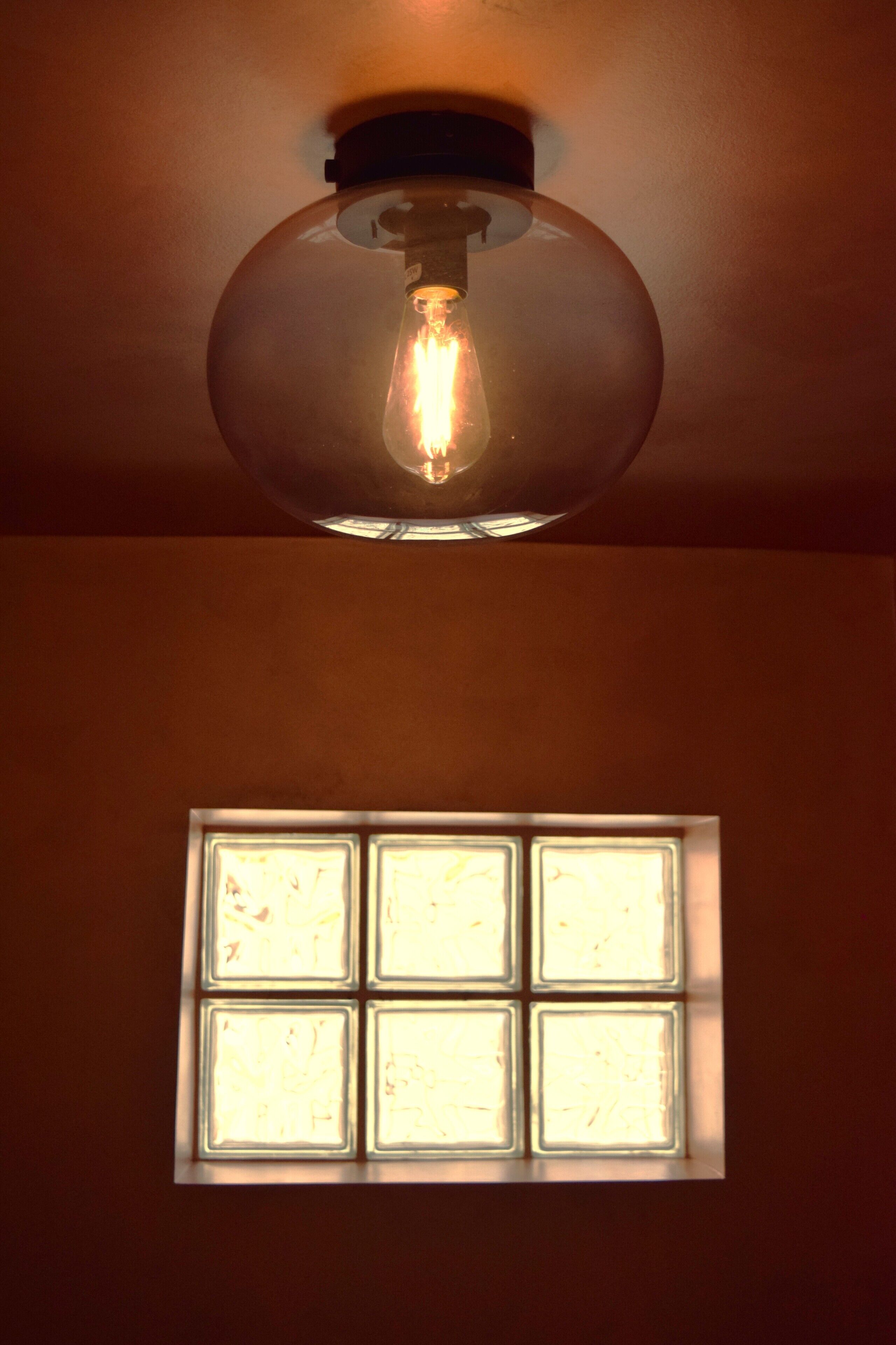 A ceiling light fixture with a visible filament bulb and a window below it.