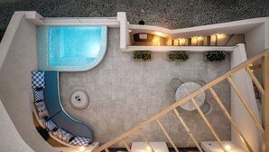 A modern interior with a swimming pool, a curved seating area, a staircase, and a dining table. - La Madeleine Suites Fira (Santorini)