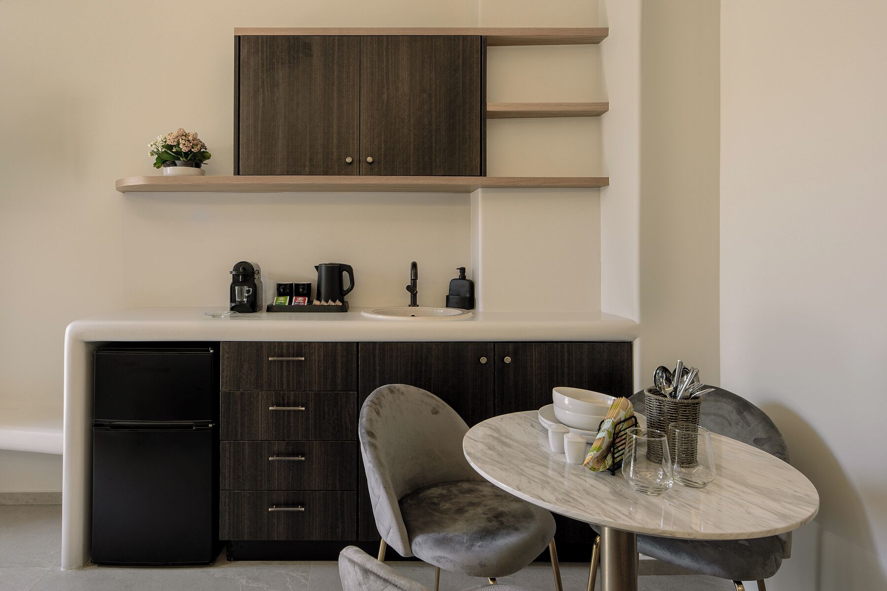 A modern kitchen with dark cabinetry, a built-in coffee maker, and a round marble table with chairs.