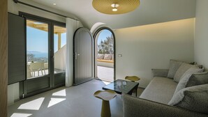 A modern interior with a dining area, a sofa set, and a view through a glass door. - La Madeleine Suites Fira (Santorini)