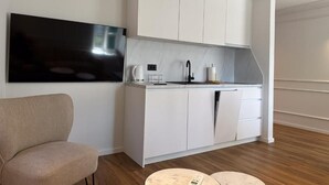Een moderne keuken met witte kastjes, een flatscreen televisie, een koffiezetapparaat en een klein, rond tafeltje.