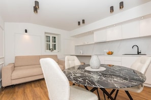 Una cocina moderna con armarios blancos, encimera de mármol y un comedor con una mesa redonda y sillas.