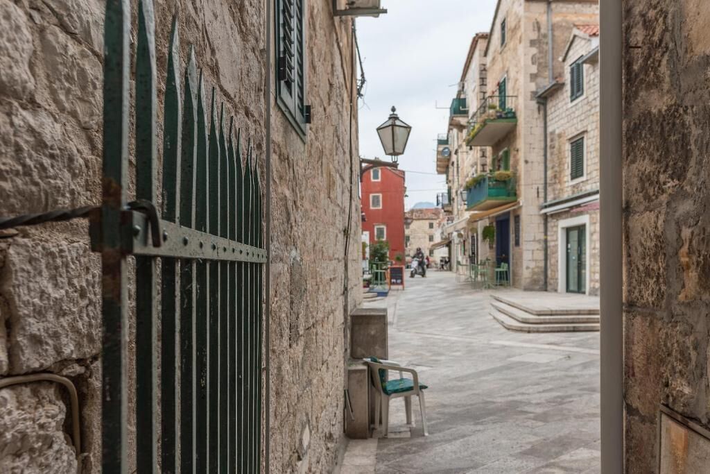 A narrow street with stone buildings, a metal gate, and a bench.