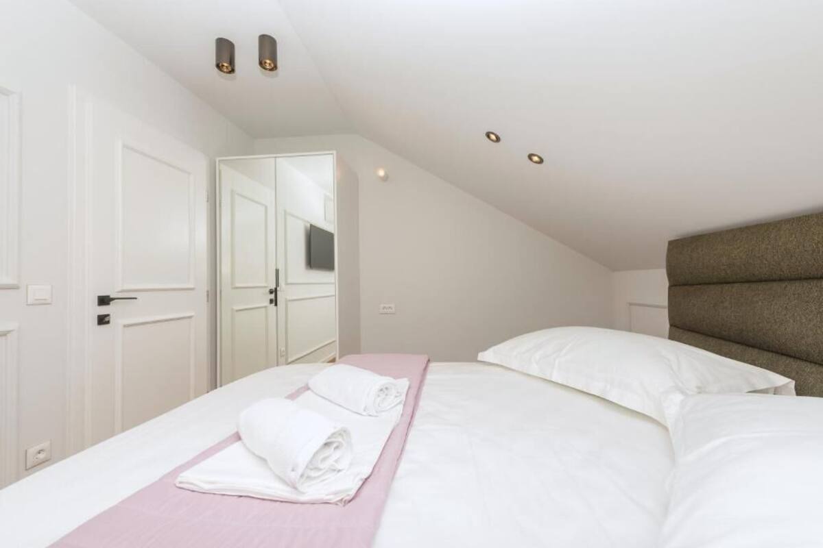 A bedroom with a bed, a bedside table, a mirror, and a door.