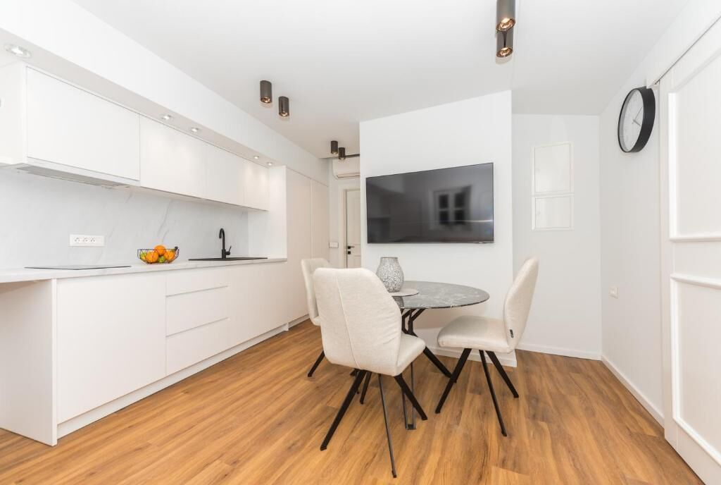 A modern kitchen with white cabinets, a dining table with chairs, and a clock on the wall.
