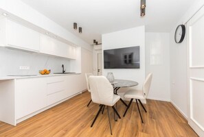Una cocina moderna con armarios blancos, una mesa de comedor con sillas y un reloj en la pared.