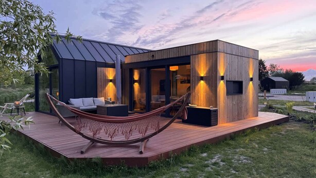 Una casa moderna con una terraza, una hamaca y una puesta de sol al fondo.