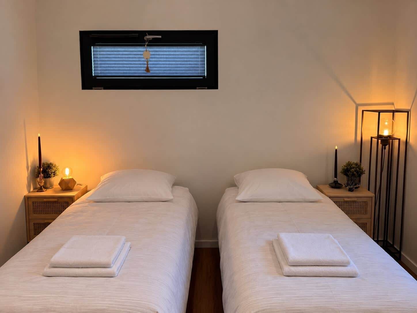 A room with two beds, a window with blinds, bedside lamps, and a floor lamp.