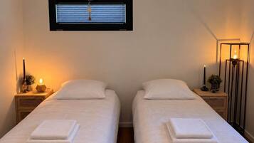 A room with two beds, a window with blinds, bedside lamps, and a floor lamp.