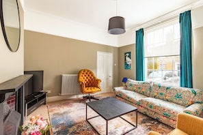 A living room with a sofa, armchair, coffee table, and a television. - A rare find: central Norwich, three-bed Victorian period home with off-street parking for two on the drive. Sunny enclosed courtyard, downstairs WC, fast fibre WiFi. Six minutes' walk to the castle, four to Chantry Place. Sleeps five. (Norwich)