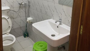 A bathroom with a toilet, sink, and green bucket. - Lillian Imperial Country Hotel (Kamuli)