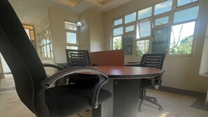 A conference room with a large table, four office chairs, and large windows allowing natural light. - Lillian Imperial Country Hotel (Kamuli)