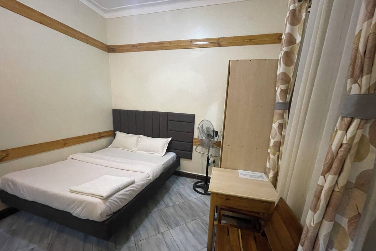 Una habitación con cama, escritorio, silla, ventilador y espejo.