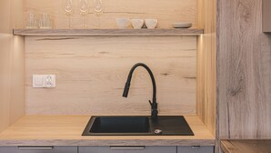 Uma cozinha moderna com pia preta, bancada de madeira e prateleira com copos e xícaras.