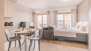 Quarto de hotel moderno com área de jantar, sofá, cama e varanda com cortinas.
