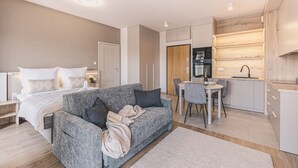 Um quarto moderno com uma cama, um sofá cinzento e uma pequena área de jantar com uma mesa e cadeiras.