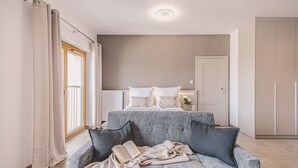 Um quarto com cama, guarda-roupa, janela com cortinas e sofá com um livro.