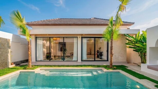 Una casa moderna con piscina, puertas de cristal amplias y palmeras.